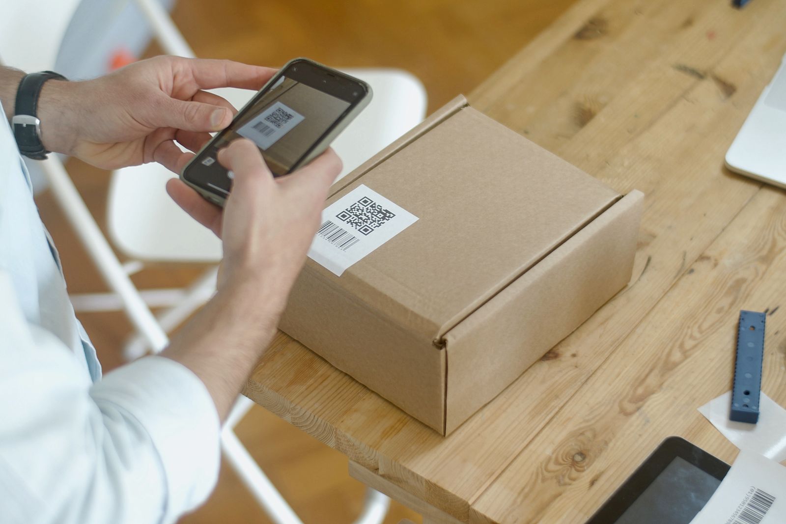 Ruky so smartfónom pri snímaní QR kódu na balíku na drevenom stole